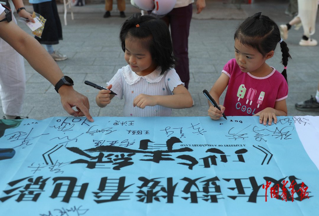 6月20日，北京鼓楼前，两位小朋友在大人的带领下准备在签名布上写上名字。中青报·中青网记者 陈剑/摄