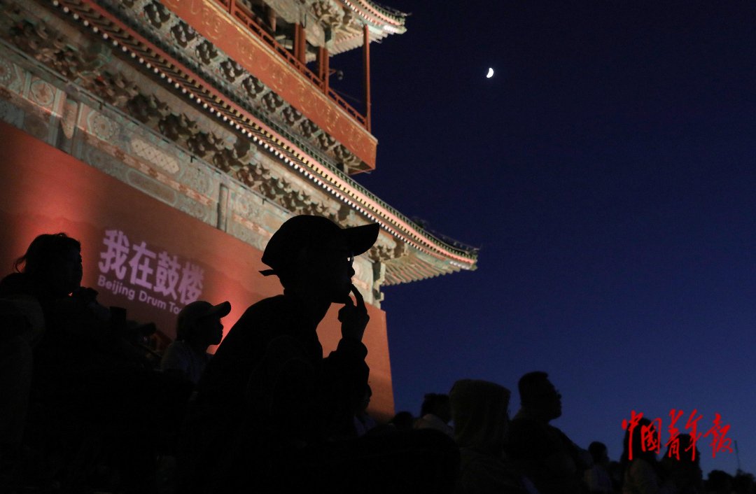 6月20日，北京鼓楼前，观众正在观看露天电影，一钩弯月挂在夜空。中青报·中青网记者 陈剑/摄