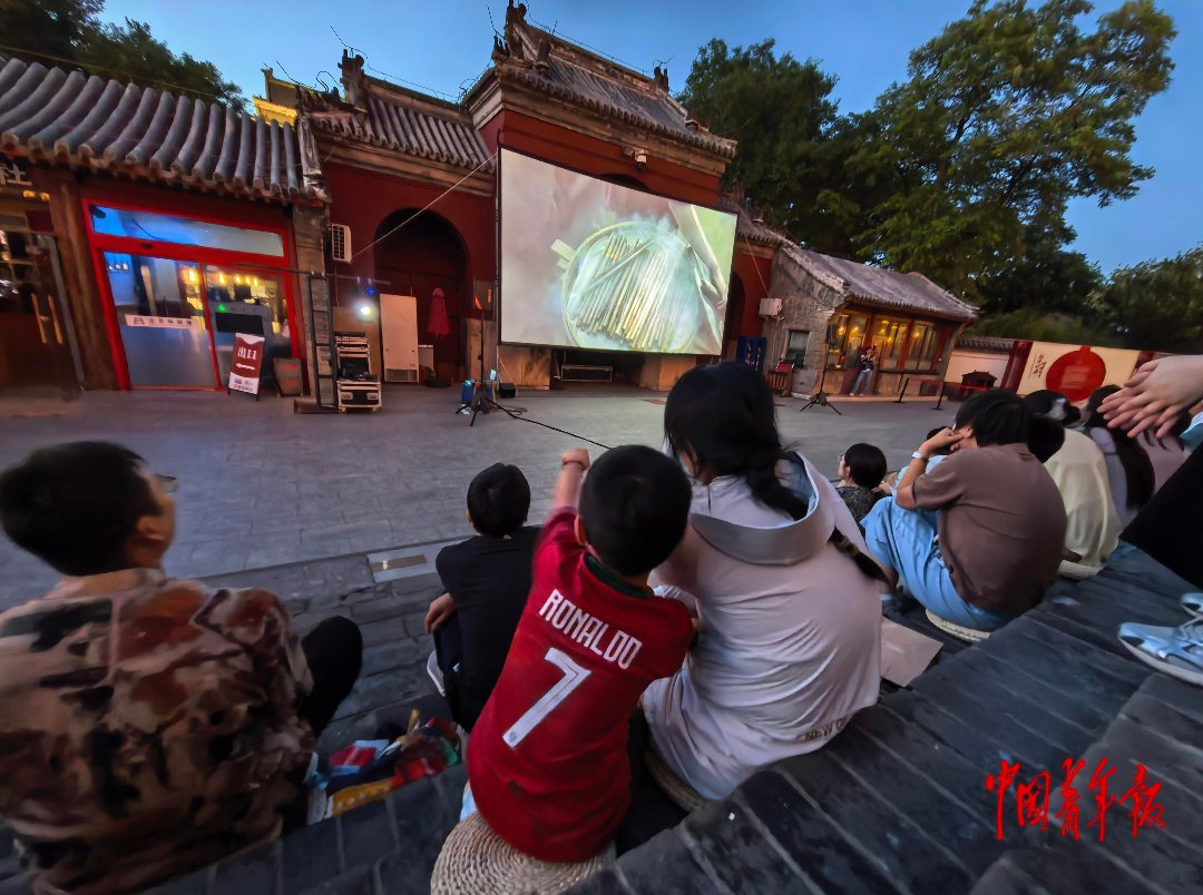 6月20日，北京鼓楼前，一位穿着“C罗”7号球衣的小朋友和家长一起坐在台阶上，观看露天电影。中青报·中青网记者 陈剑/摄