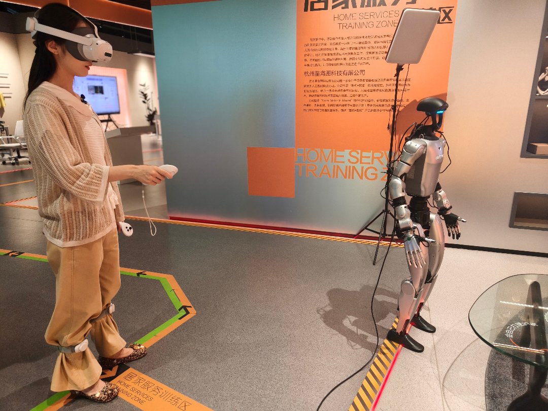 7月29日，杭州市具身智能展示与应用推广中心二楼，在居家服务模拟场景展示区，随着参观者戴上了VR眼镜手持设备开始做动作，旁边的机器人也将学习这组动作。中青报·中青网记者 宁迪/摄