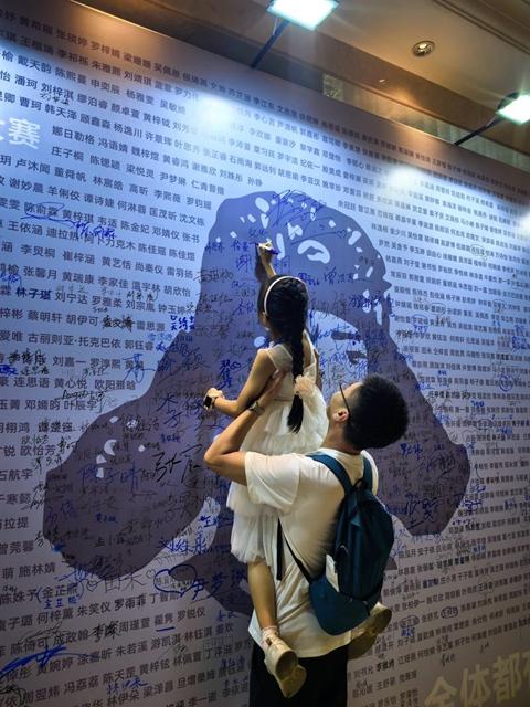 在大赛现场，小选手被父亲托举着在印有自己名字的展板上签字。大赛组委会供图