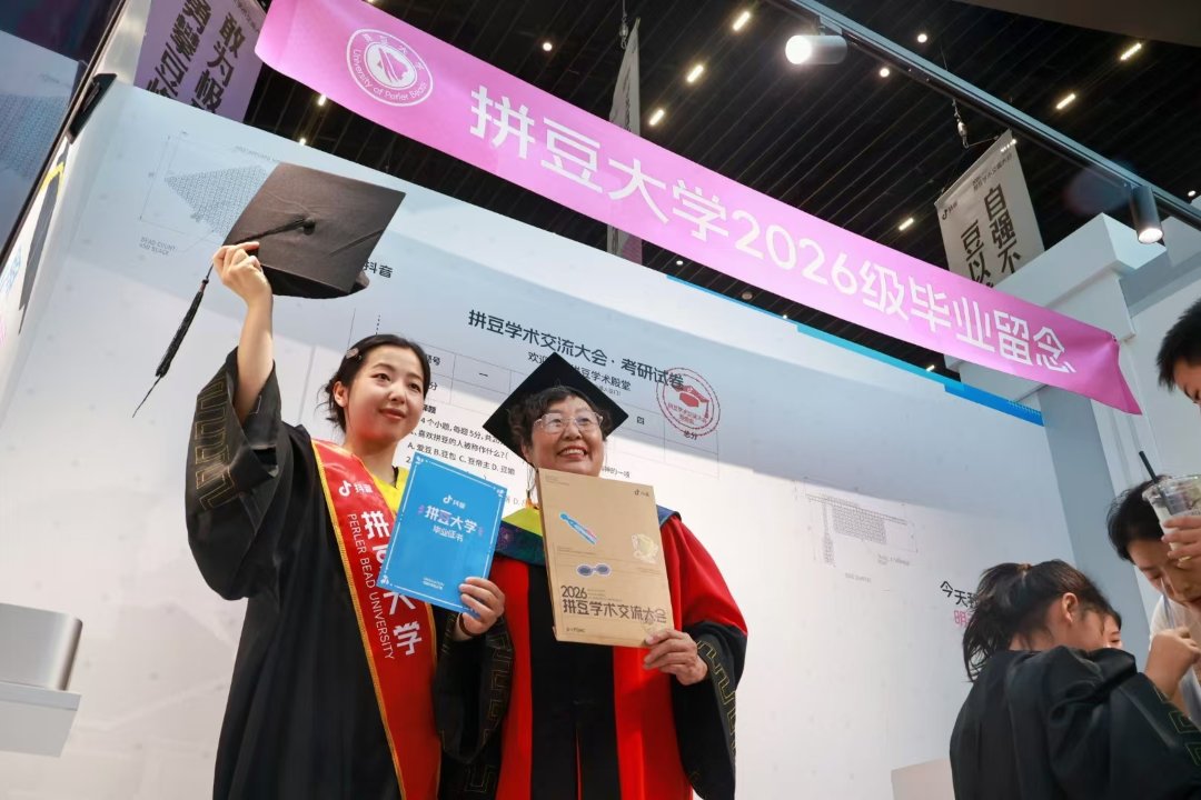 9月12日，北京市西城区，拼豆学术交流大会现场，一位年轻人身着“学位服”，与拼豆大学“校长”在横幅下合影留念。9月10-13日，一场别开生面的拼豆学术交流大会在当地一处商场举行。现场不仅有由260万颗豆子拼接而成的巨幅《清明上河图》，200多个国内优质拼豆作品，还集中展出各类拼豆熨烫工艺与主题创意作品，吸引大批爱好者前来观展和参与互动体验。据介绍，近年来，拼豆凭借解压属性、灵活的图案创作方式与较低的入门门槛，收获不少年轻人的喜爱。张旭冉/摄