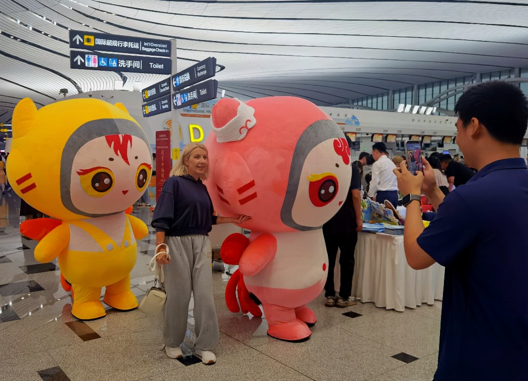 9月24日，北京大兴国际机场，航旅嘉年华现场，一名外国游客与三亚凤凰国际机场吉祥物“菲菲”“尼克斯”合影。李庚伟/摄