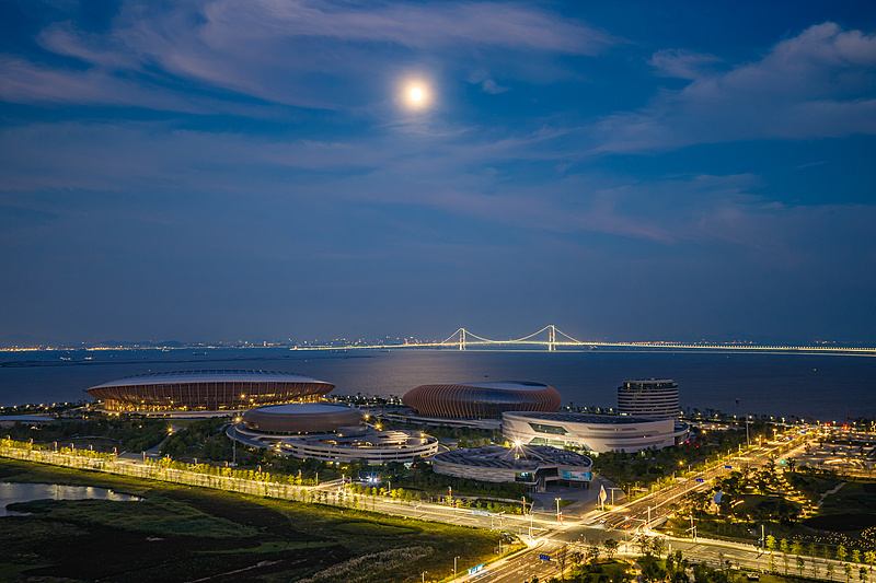 2026年9月25日，广州南沙，中秋节傍晚，一轮明月在广州南沙大湾区体育文化中心上空升起，与远处的深中通道同框。