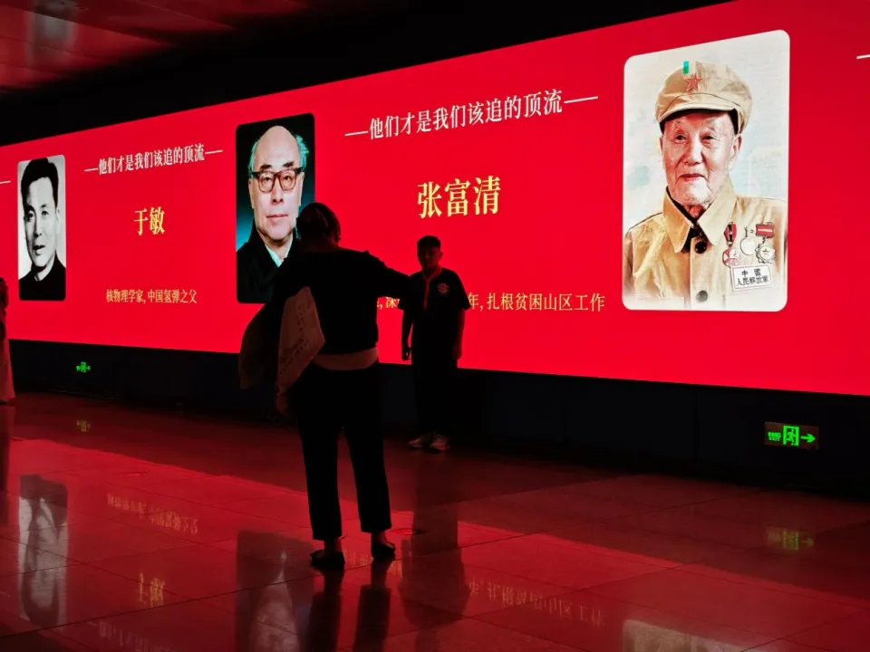 10月1日，在郑州地铁会展中心站，一位小朋友正站在科学家海报前拍照。新华社记者 刘振坤 摄