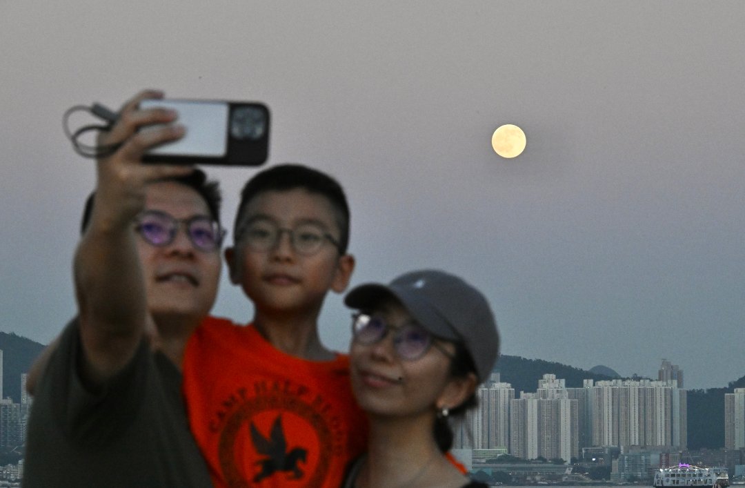 9月26日,农历八月十六,中国香港,维多利亚港上空升起一轮明月,一家三口与圆月合影。视觉中国供图