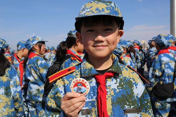 　　2026年9月，黑龙江省黑河市第六小学教育集团举办“国防教育少年军校拓展训练营重走长征路”主题拉练活动。450个孩子徒步拉练，沿途设了湘江战役、遵义会议、翻越雪山等6个长征打卡点。老师边走边讲那段历史。图为9月14日六(2)中队刘诗腾同学在顺利“会师”后展示活动纪念徽章。解欣供图