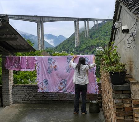 2026年5月16日，贵州省遵义市习水县土城镇，一位居民正晾晒被单，不远处的蓉遵高速土城特大桥从云雾缭绕的青山中飞跨赤水河。中央红军曾在土城进行了惨烈的青杠坡战斗，一渡赤水河，拉开了“四渡赤水”的序幕。如今，土城依托红色文化与生态资源发展旅游业，成为贵州省第一批乡村旅游重点镇。